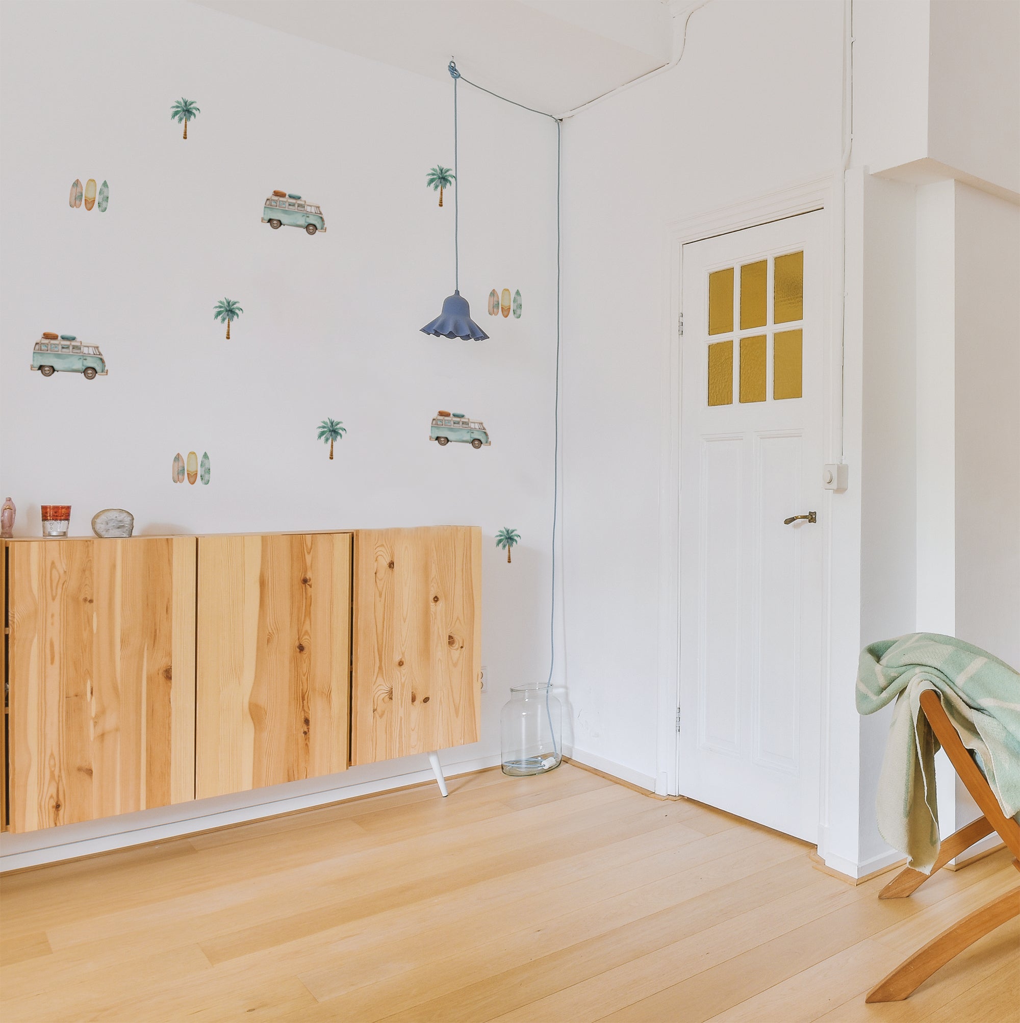 Detalle de pared de salón con estilo surfero, decorada con vinilo decorativo Salinas, compuesto de furgonetas, palmeras y tablas de surf con acabado efecto acuarela. Adhesivo de alta calidad fácil de colocar y de retirar - Nicolasito.es