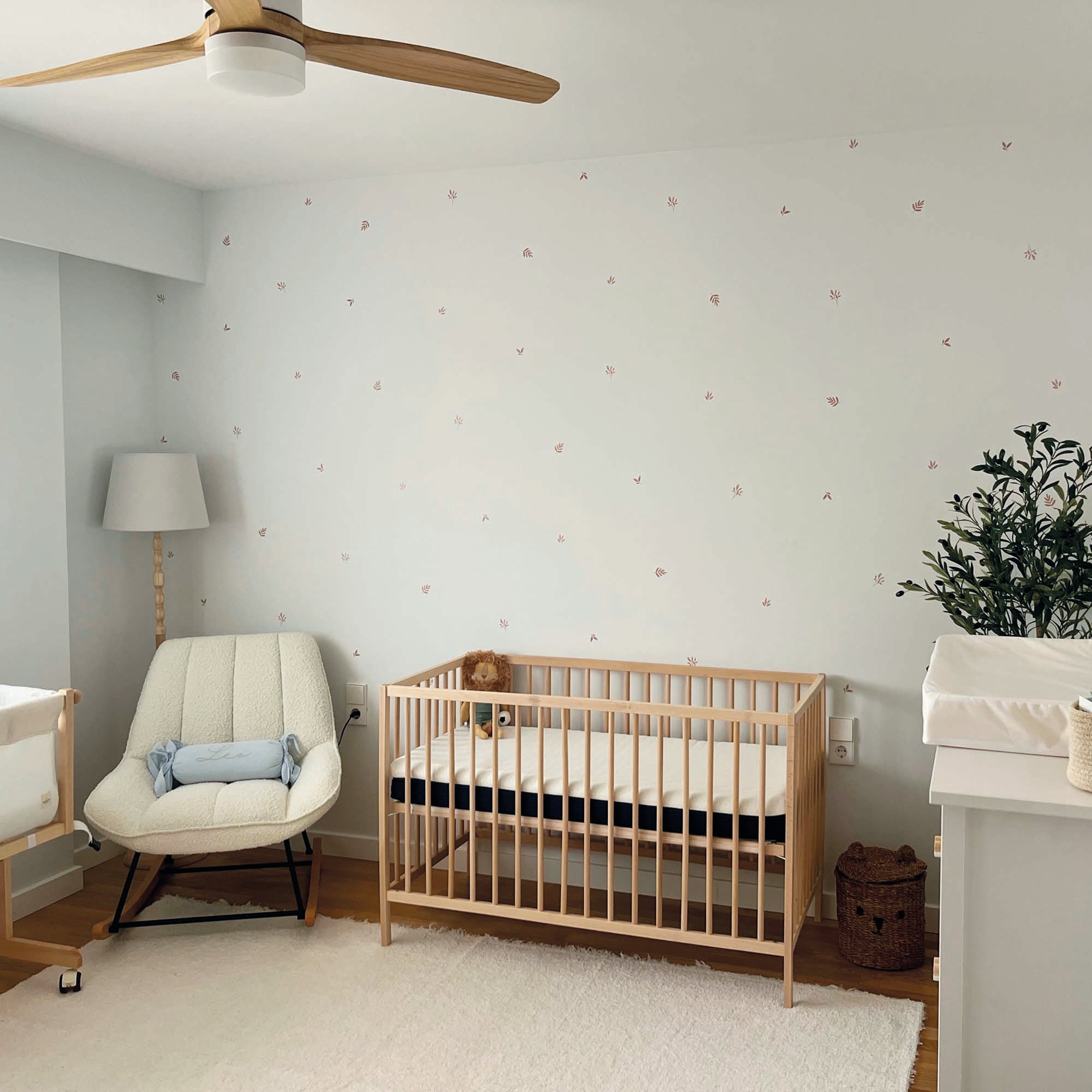 Vista general de habitación de bebé con vinilos de plantas en tonos marrón aplicados sobre pared blanca, creando un ambiente natural y acogedor. Cuna de madera en habitación de bebé con pared decorada con vinilos de hojas en acuarela marrón, simulando papel pintado botánico. Nicolasito.es #color_plantas-acuarela-marron
