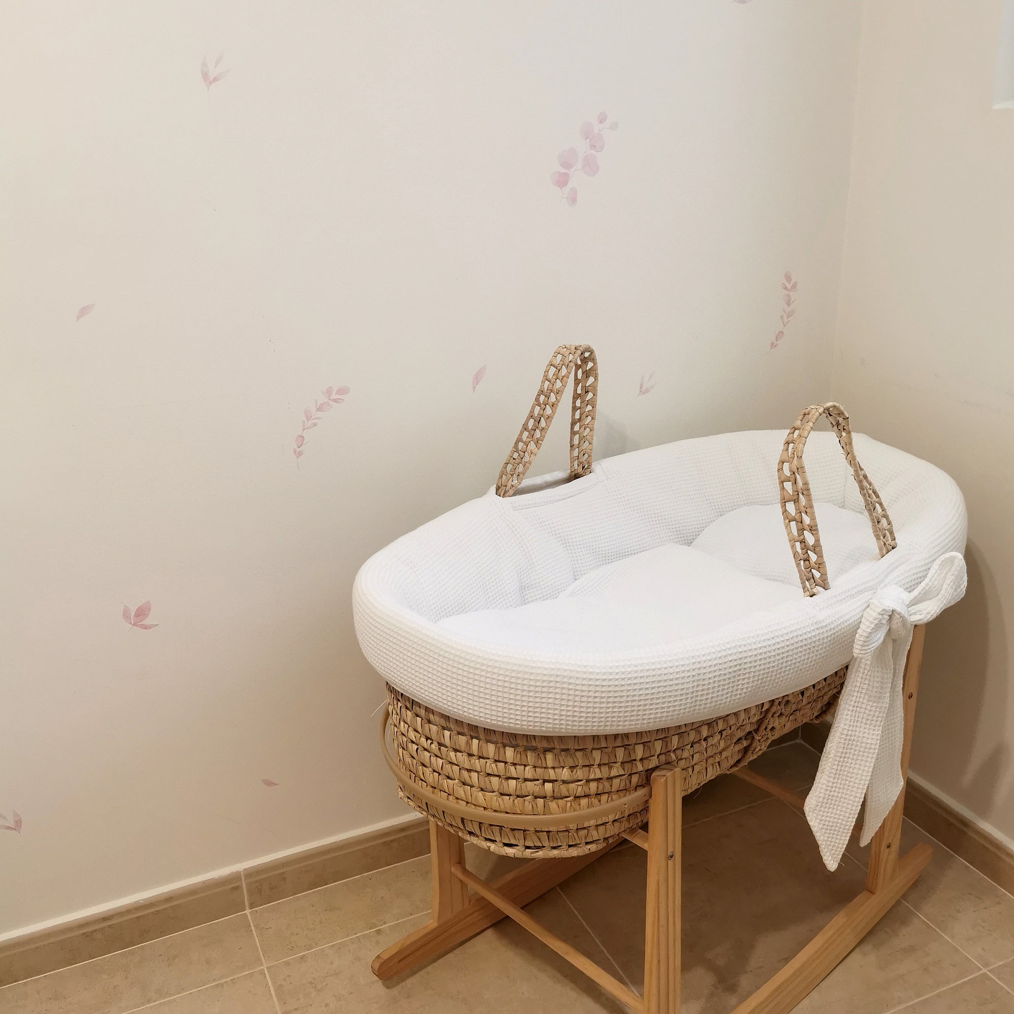 Dormitorio infantil con cuna de mimbre y madera y paredes blancas decoradas con cinilo decorativo en forma de plantas de eucalipto en color rosa creando un ambiente elegante - Nicolasito.es #color_plantas-eucalipto-rosa