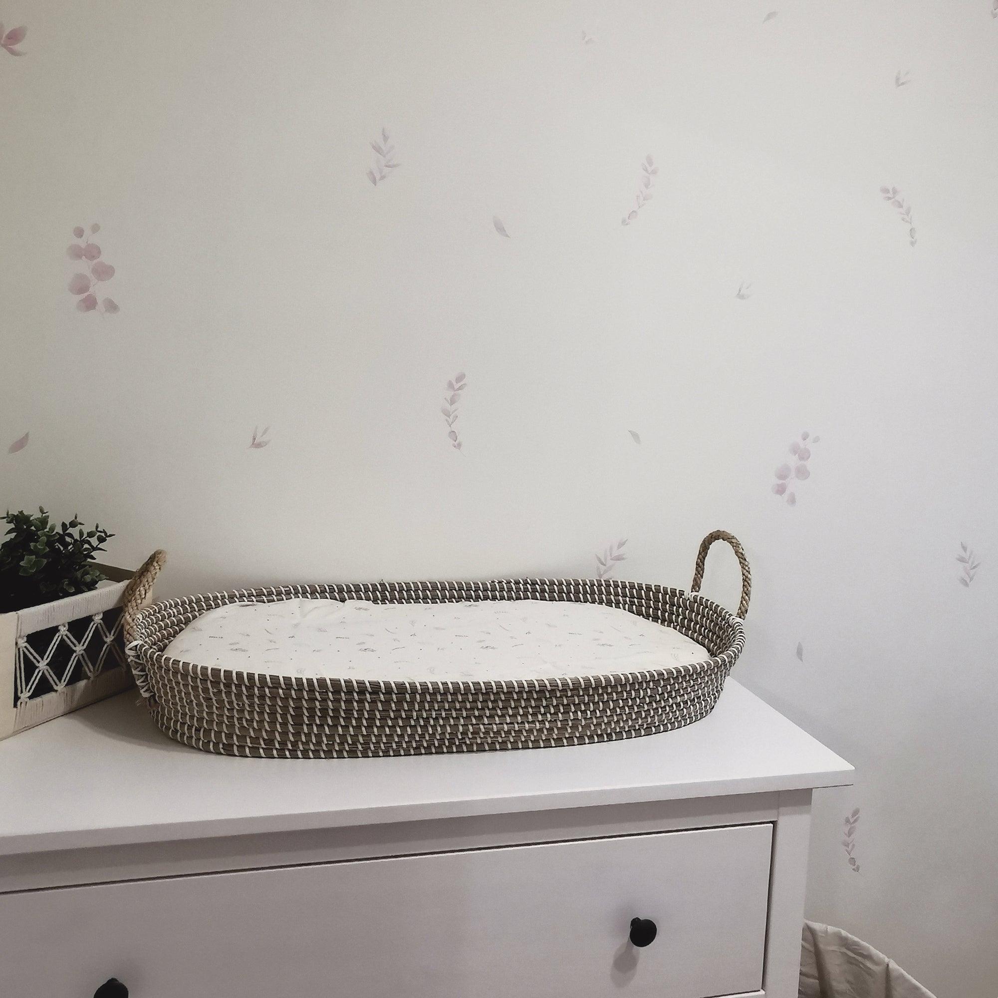 Zona de cambiador del bebé con detalles en madera y de mimbre. Estancia decorada con vinilo decorativo de paredes adhesivo en forma de plantas eucalipto de color rosa creando un efecto papel pintado elegante - Nicolasito.es #color_plantas-eucalipto-rosa