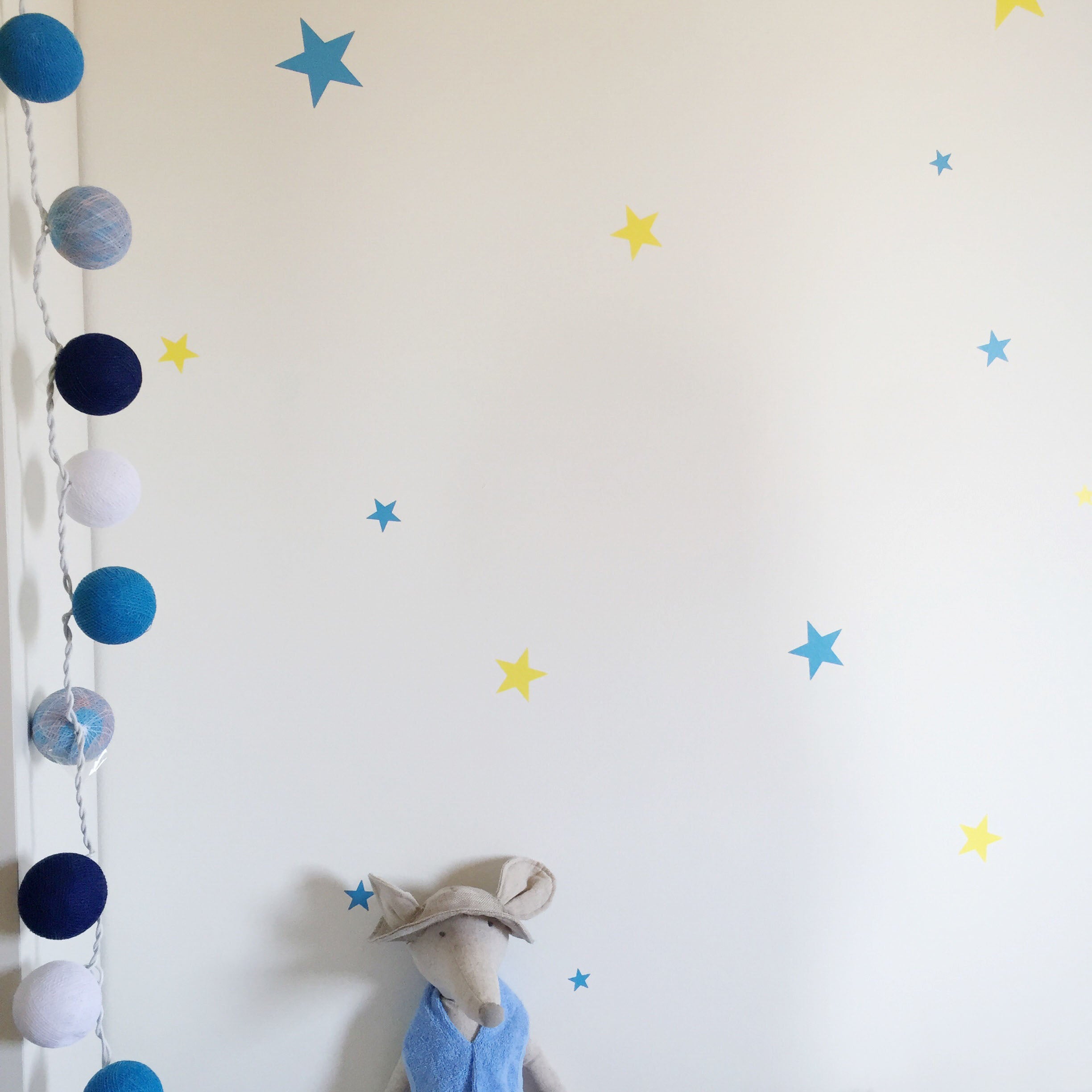 Detalle del vinilo decorativo de paredes en forma de estrellas azules y amarillas de varios tamaños sobre pared lisa y blanca y dormitorio - Nicolasito.es #color_Amarillo