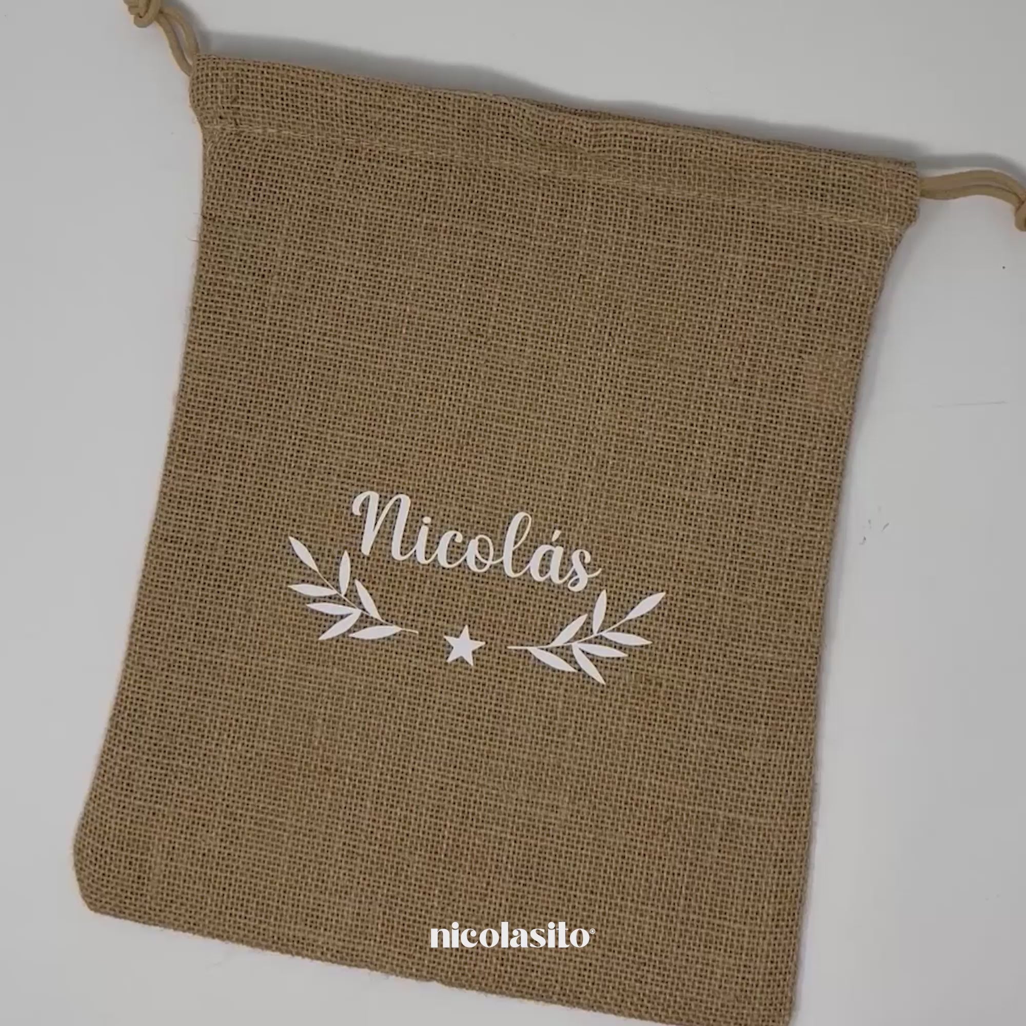 Vídeo del saco de Navidad de yute personalizado mostrando el modelo en color blanco, personalizado con nombre o frase en vinilo textil. Perfecto para guardar regalos, decorar el árbol o la chimenea y crear una Navidad sostenible y con estilo. Hecho con yute natural resistente y reutilizable año tras año - Nicolasito.es