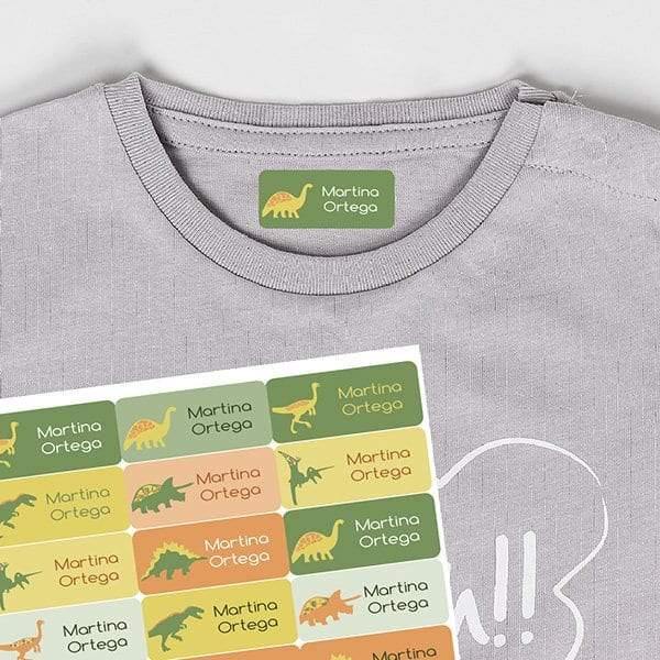 Plano detalle de etiquetas termoadhesivas para la ropa con ilustraciones de dinosaurios en color verde sobre cemiseta de algodón, resistentes al lavado y al roce diario; se entregan 25 unidades personalizadas con nombre - Nicolasito.es #color_Verdes