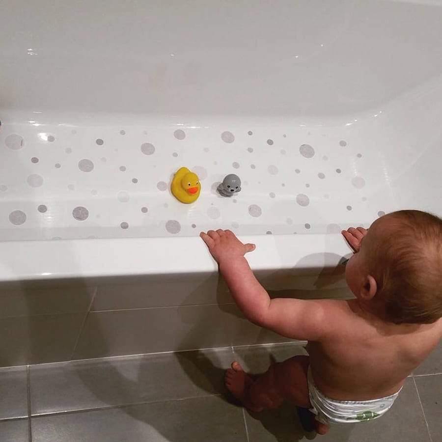 Bebé mirando una bañera con pegatinas de burbujas decorativas color gris en el fondo y patito amarillo, esperando para disfrutar de un baño seguro y divertido. Antideslizante burbujitas - Nicolasito.es #color_Gris Claro