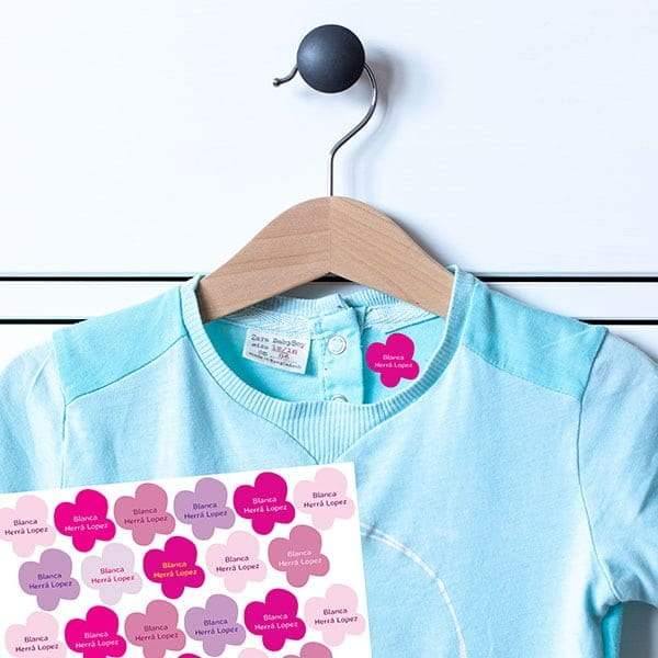 Imagen dónde se muestra cómo quedan las etiquetas con diseño de mariposas en color rosa ya adheridas a una camiseta azul de algodón, ideales para uniformes. Su adhesivo es duradero y son fáciles de aplicar con una plancha de uso doméstico - Nicolasito.es #color_Rosa