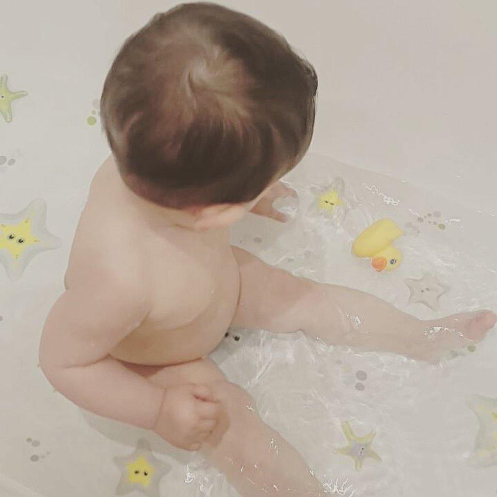 Imagen de un niño pequeño jugando dentro de una bañera llena de agua sobre la que se colocan pegatinas antideslizantes en forma de estrellas de mar de color verde y creando un ambiente divertido y seguro sin resbalones durante el baño - Nicolasito.es #color_Verde