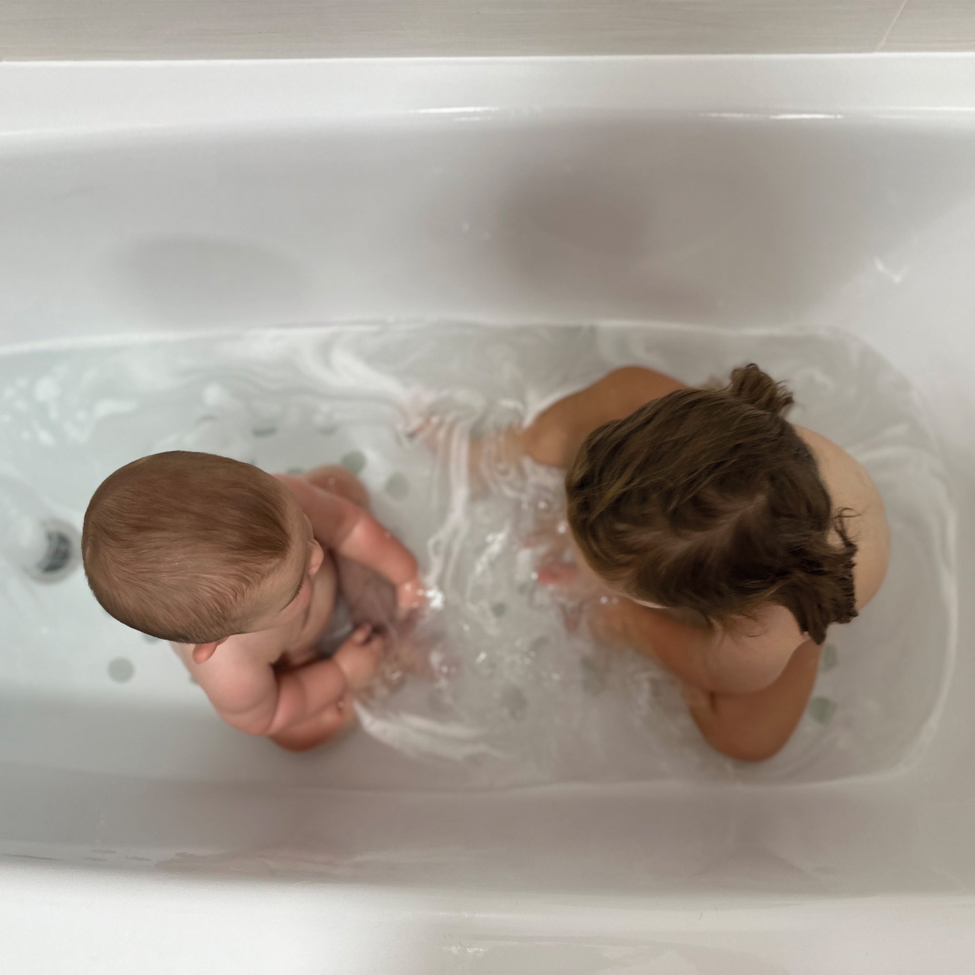Niños jugando en una bañera con pegatinas de topitos antideslizantes de color gris en el fondo, disfrutando  de un baño seguro y divertido. Antideslizante topitos acuarela - Nicolasito.es #color_antideslizante-topitos-gris